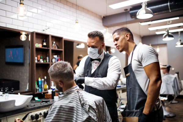 Handsome hipster man client visiting haidresser and hairstylist in barber shop, training concept.