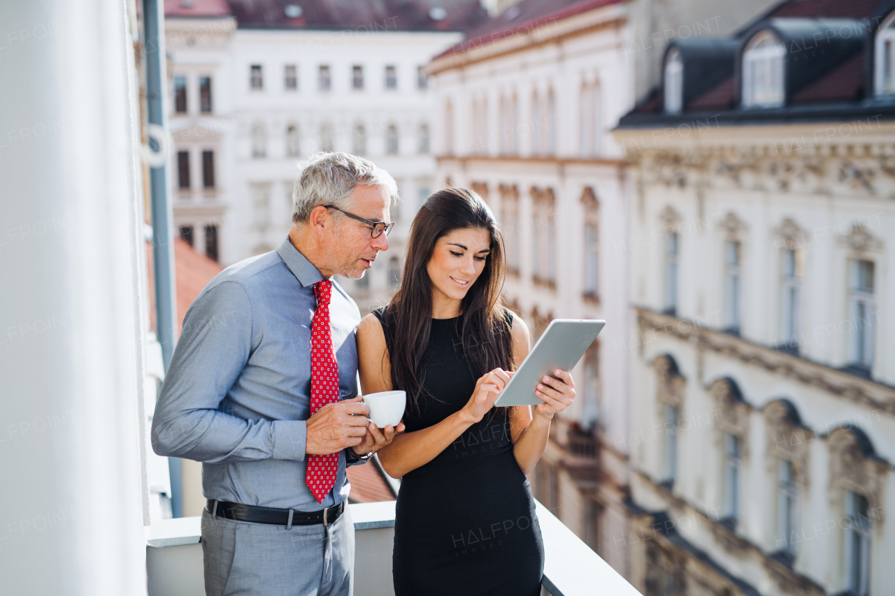 Man and woman business partners with tablet standing on a terrace in office in city, talking.