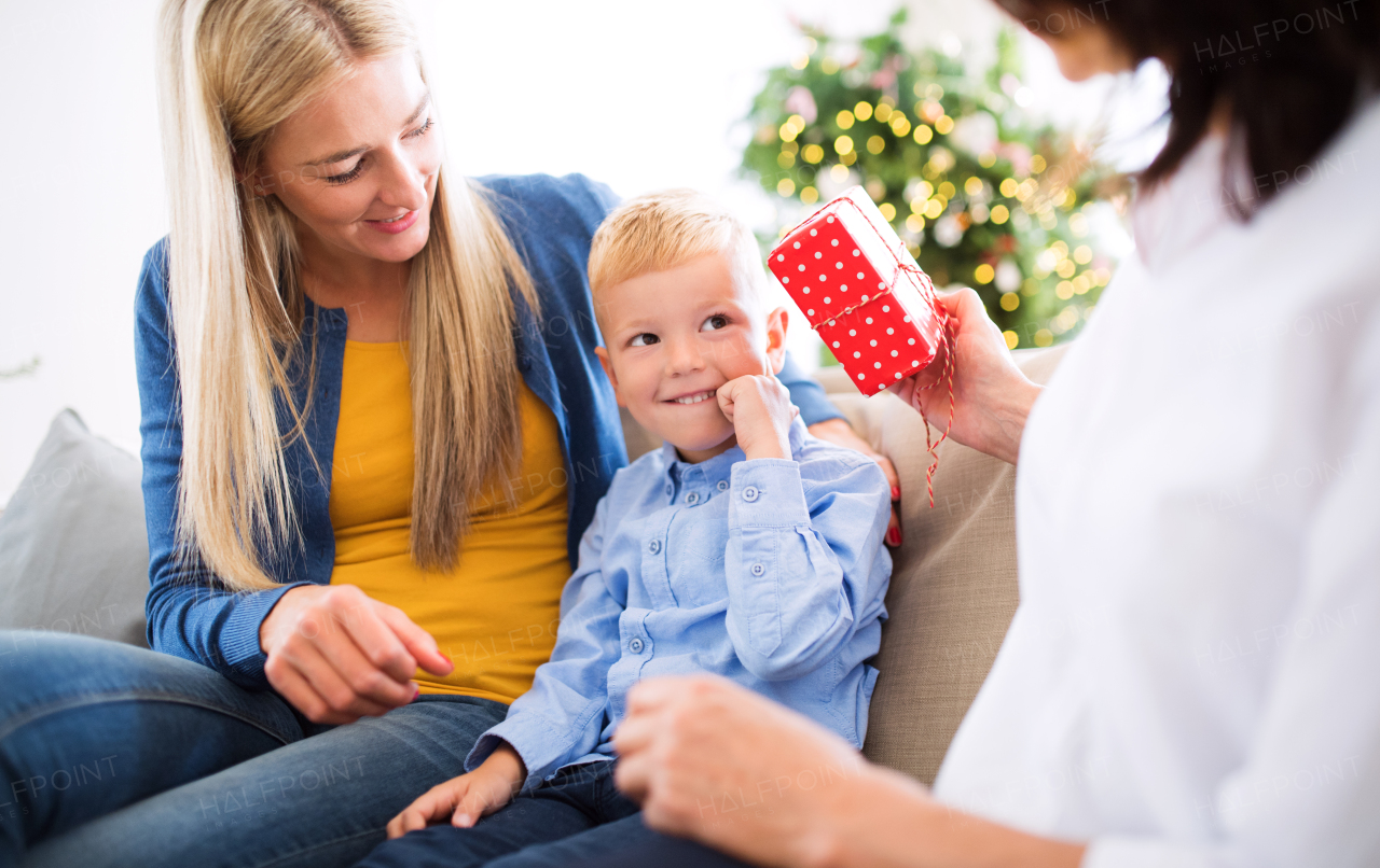 A mother and unrecognizable grandmother giving presents to a happy small boy at home at Christmas time.