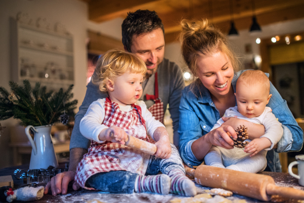 Beautiful young family making cookies at home. Father, mother, toddler boy and baby having fun.