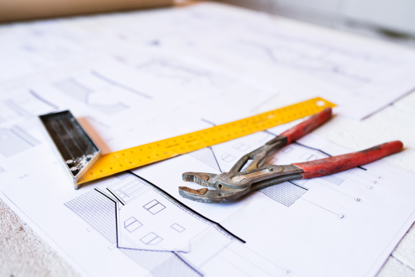 Close up of pliers, square ruler and blueprints on construction site