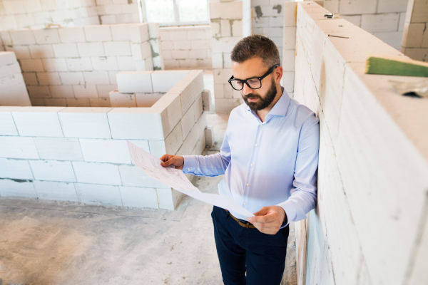 Young hipster architect or home owner at the construction site looking at blueprints, controlling issue.