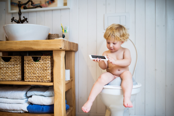 Cute toddler with a smartphone in the bathroom. Little boy sitting on the toilet.