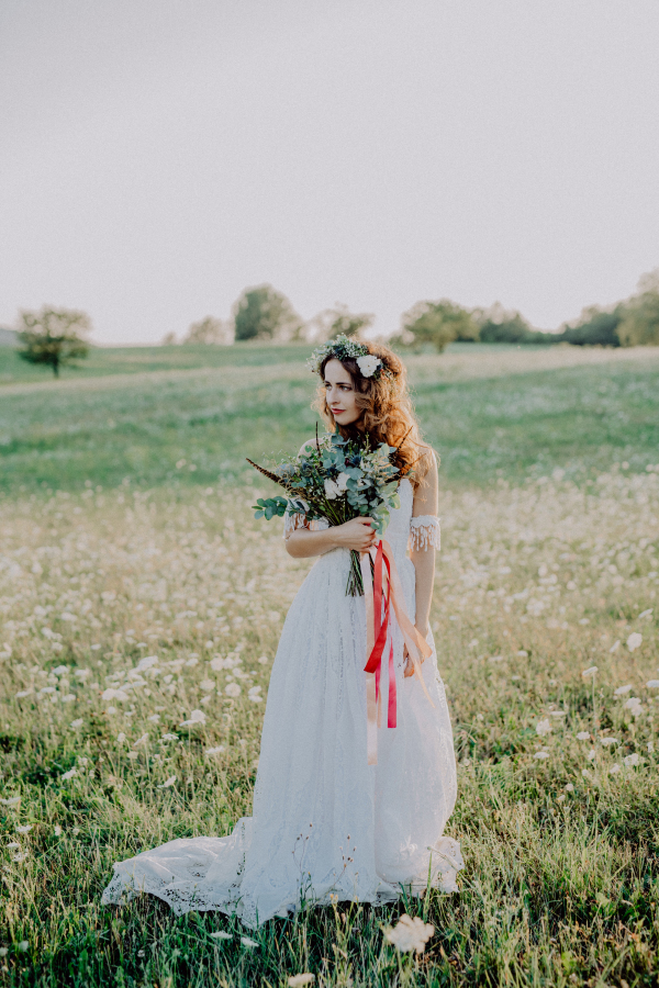 Beautiful young bride with flower wreath outside in green nature at sunset.