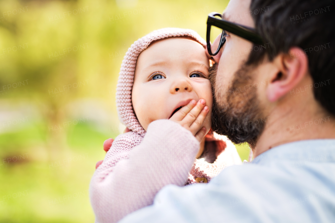 An unrecognizable father with his toddler daughter outside in green sunny spring nature, kissing.