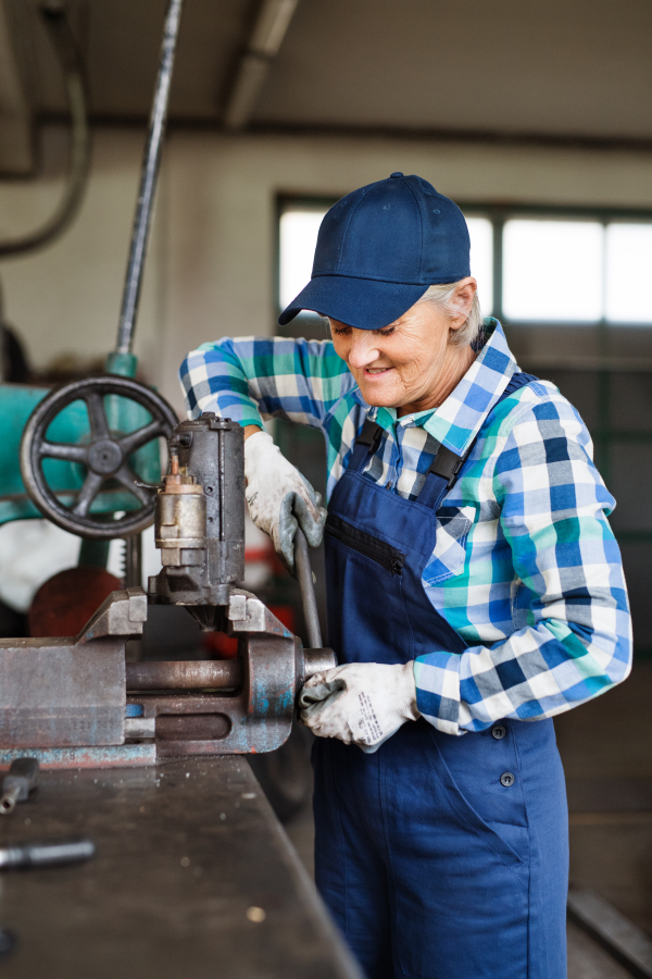 Female mechanic repairing a car. A senior woman working in a garage.