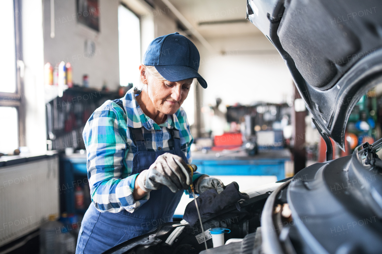 Female mechanic repairing a car. A senior woman working in a garage.