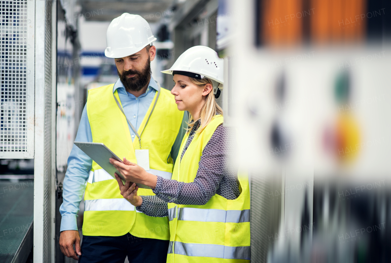 A portrait of a mature industrial man and woman engineer with tablet in a factory, talking.