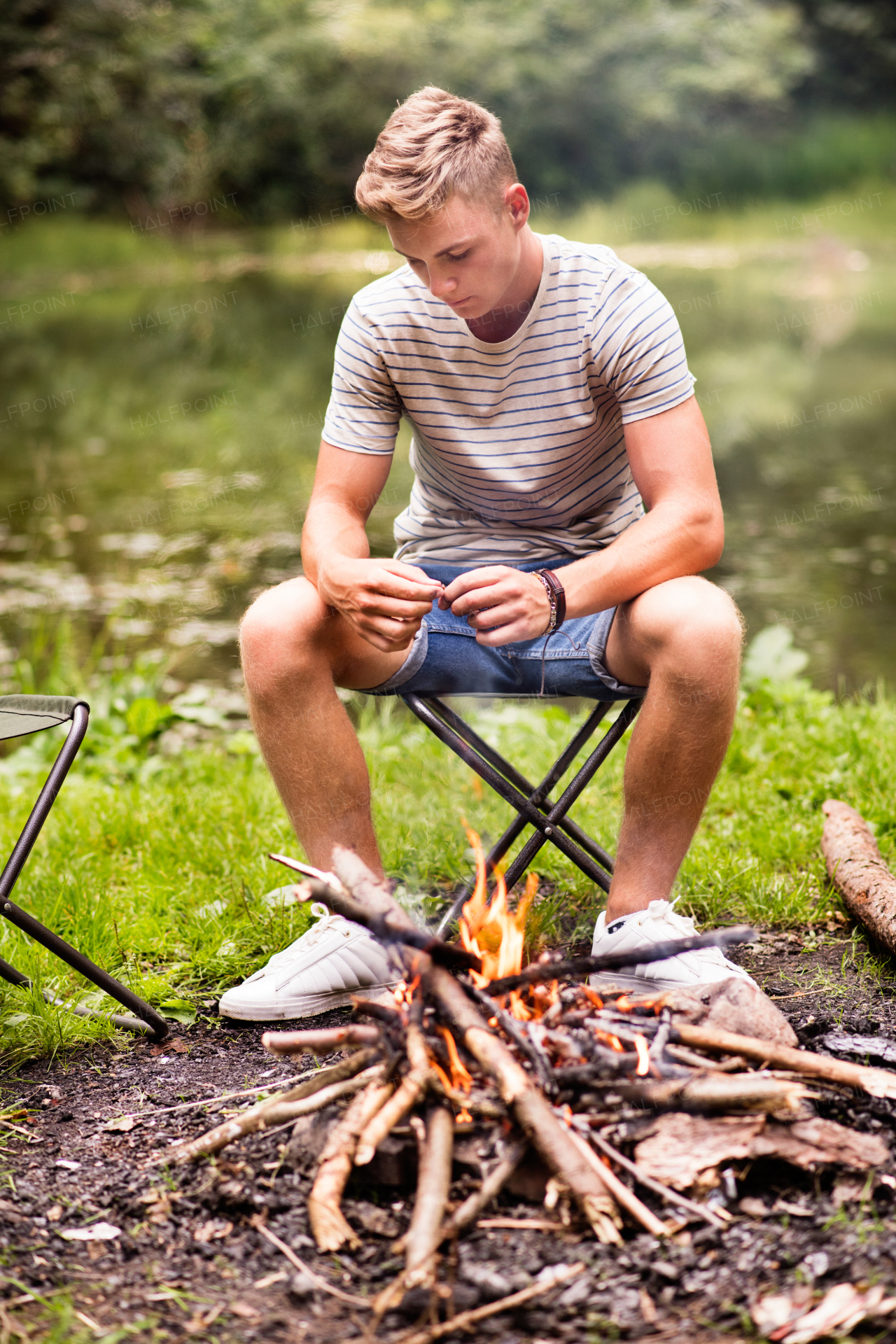Teenage boy enjoying camping vacations in forest, sitting at bonfire.