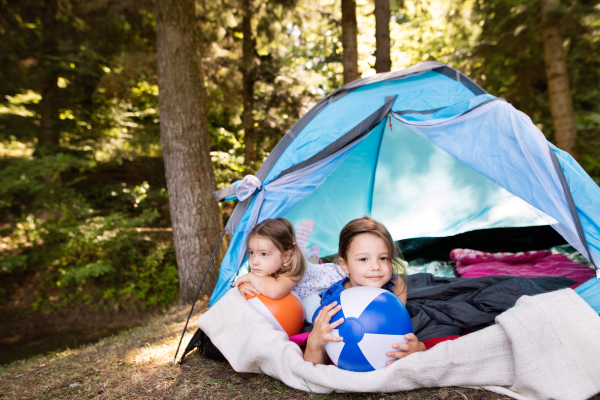 Two beautiful little girls with colorful beach balls sitting in tent, camping in the forest.