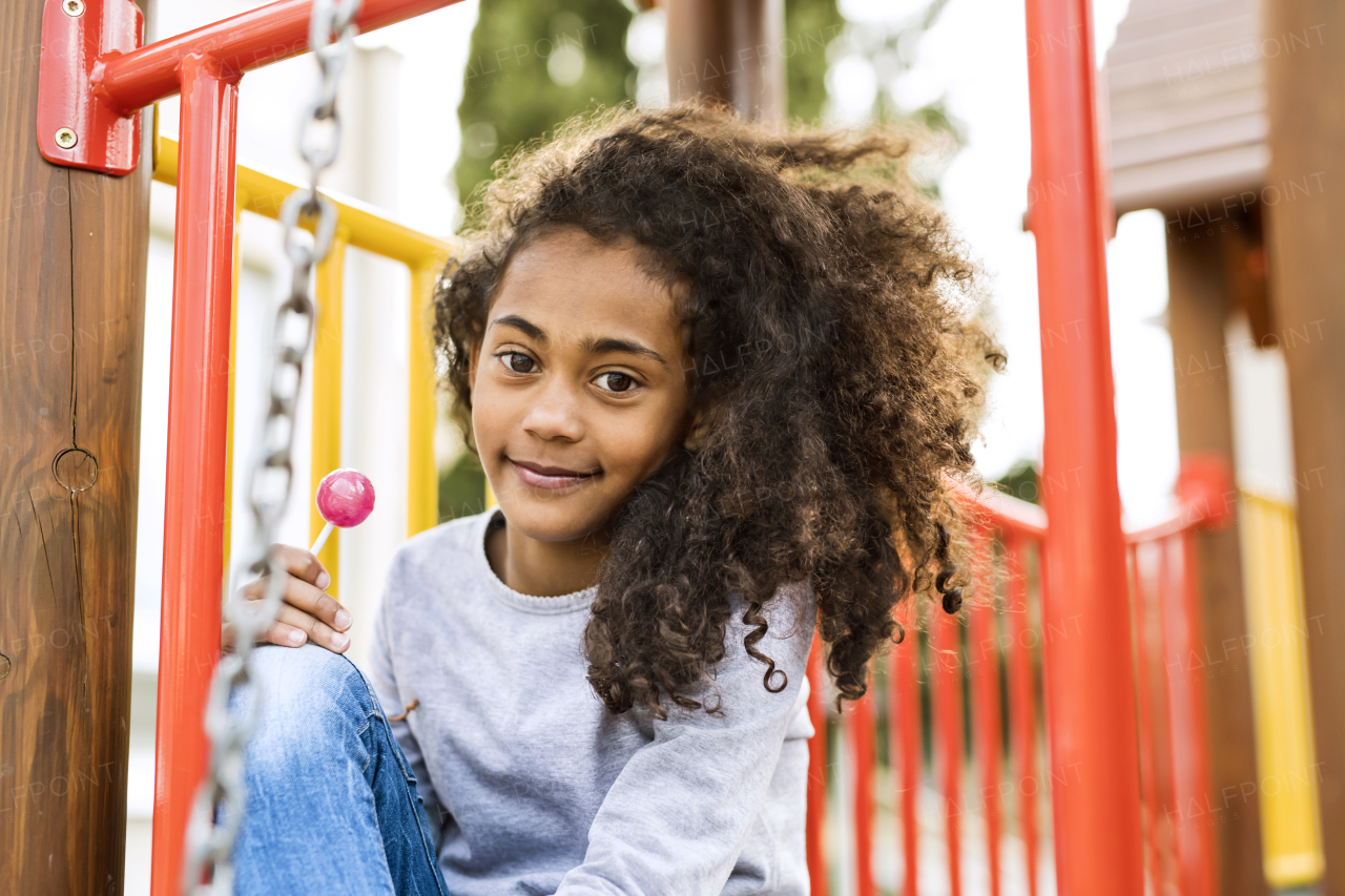 Beautiful african american girl on playground eating lollipop.