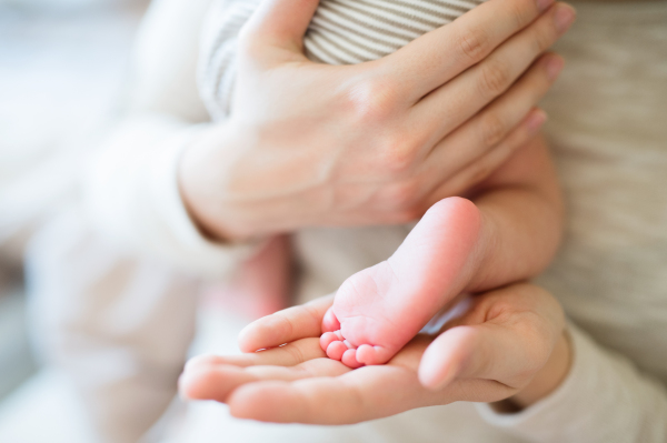 Unrecognizable mother holding her newborn baby son in her arms, close up of legs and hands.