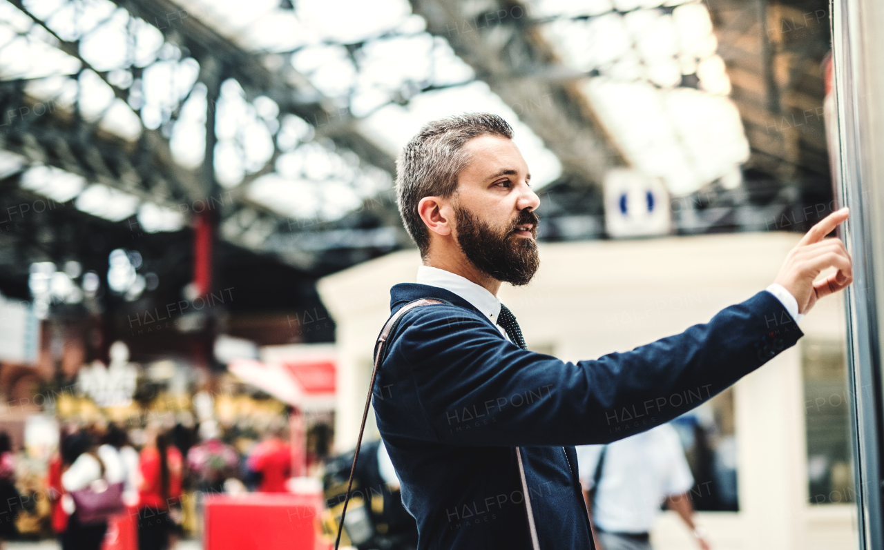 Side view of hipster businessman standing on bus or train station, checking timetable.
