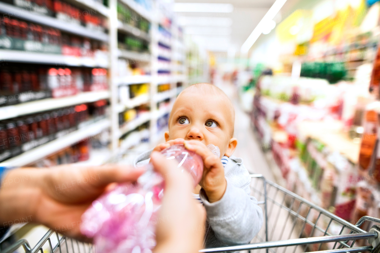 Unrecognizable young mother with her little baby boy at the supermarket, shopping. Toddler drinking.