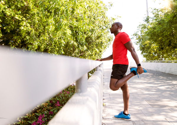Young afro-american runner in the city at the concrete wall, stretching his legs.