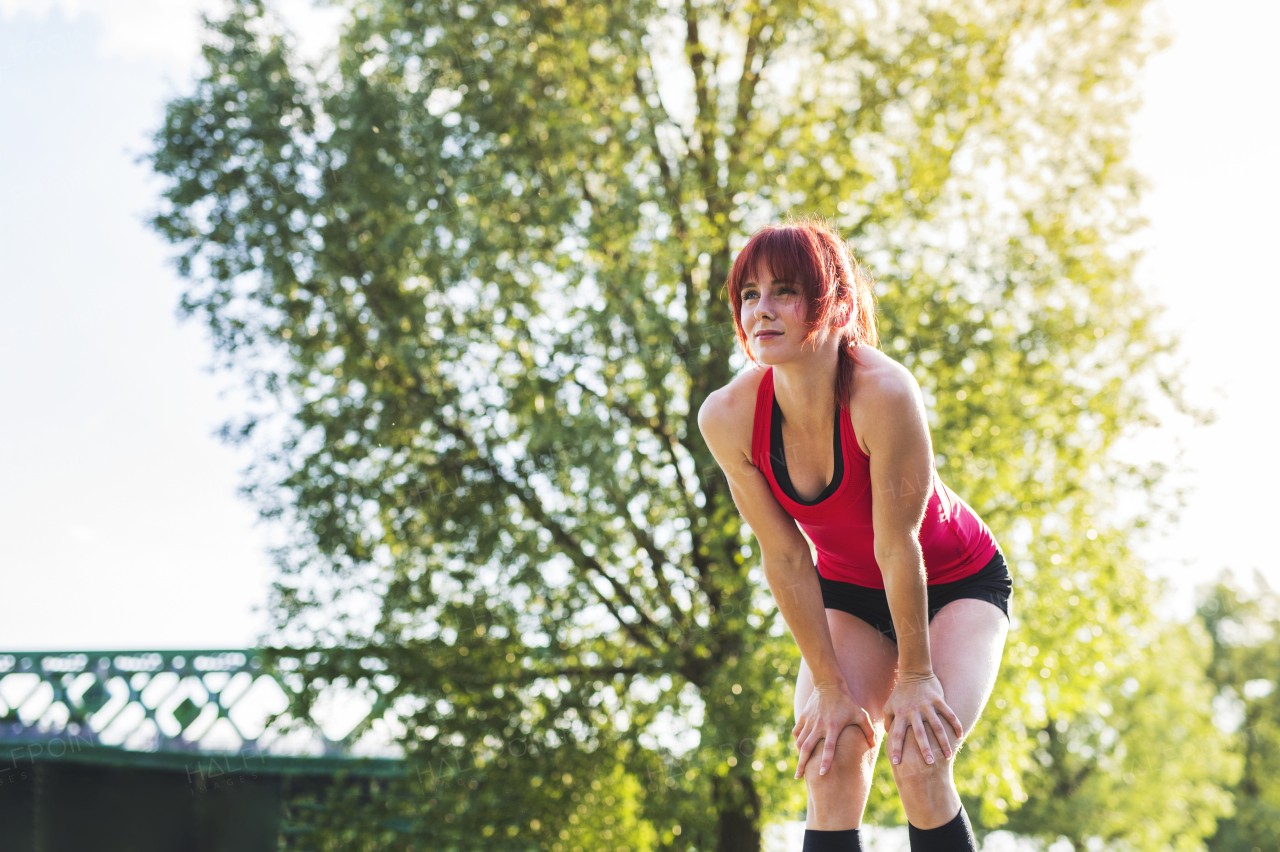 Beautiful young runner in sports clothes running in the city park, resting.