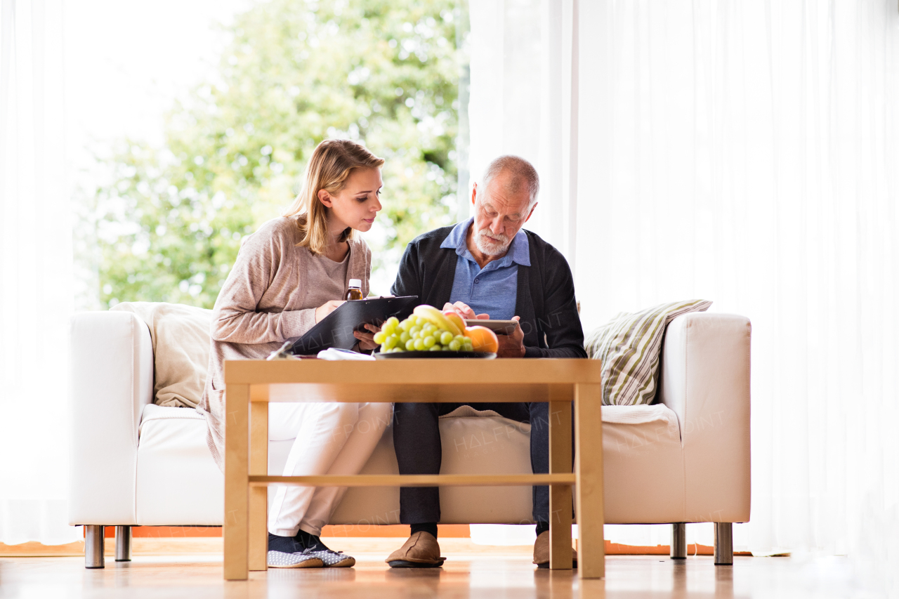 Health visitor and a senior man during home visit. A female nurse or a doctor showing test results on a tablet.