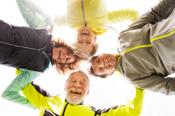 Group of active senior runners outdoors resting, arms around shoulders.