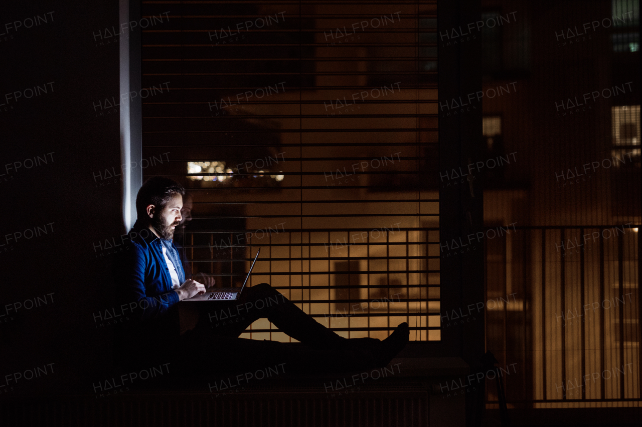 A handsome man working on a laptop at home or in an office at night.