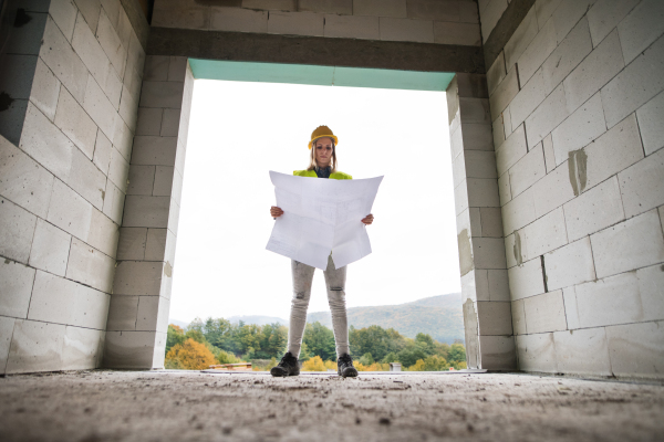 Female worker on the building site. Beautiful young woman holding blueprints. House construction.