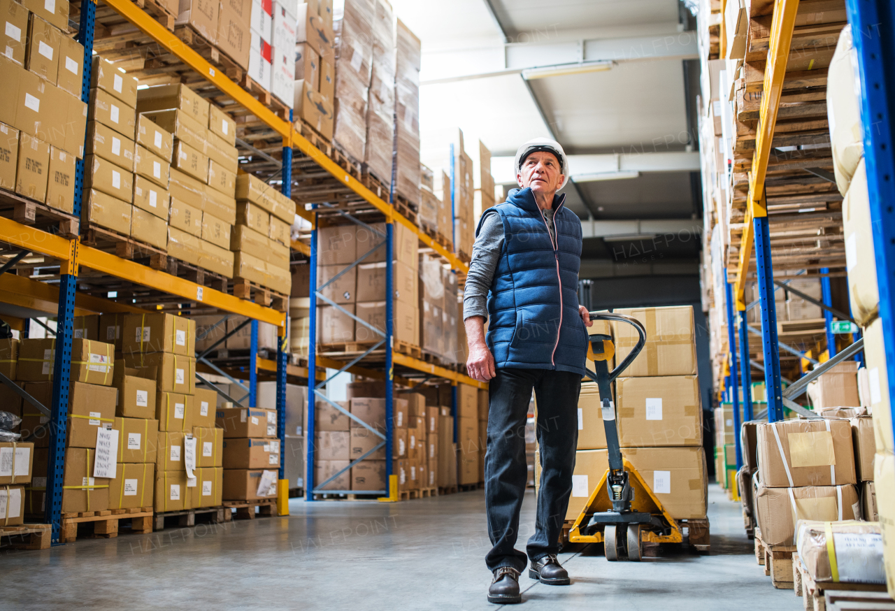 Senior male warehouse worker pulling a pallet truck with boxes.