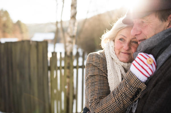 Beautiful senior woman and man on a walk in sunny winter nature hugging.