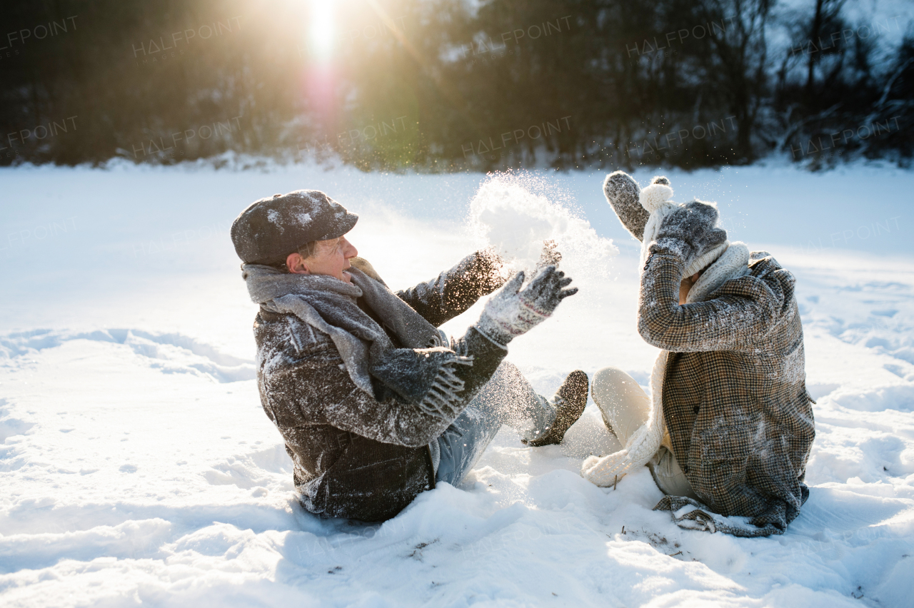 Beautiful senior woman and man on a walk in sunny winter nature, enjoying snow and having fun.