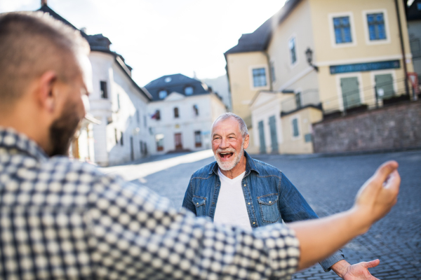 An unrecognizable adult hipster son and his overjoyed senior father in town, greeting.