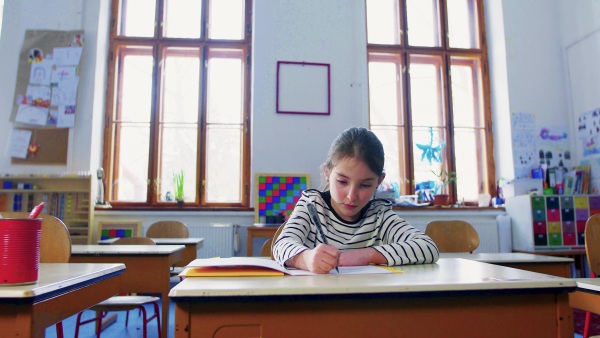 A small girl sitting at the desk at school writing.