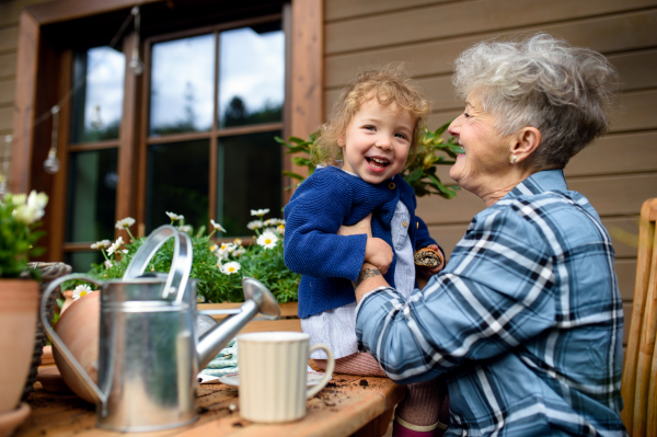 Happy senior grandmother with small granddaughter gardening on terrace in summer.