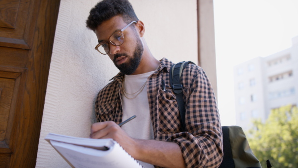 Young african-american student preparing for exam in front of the university building.