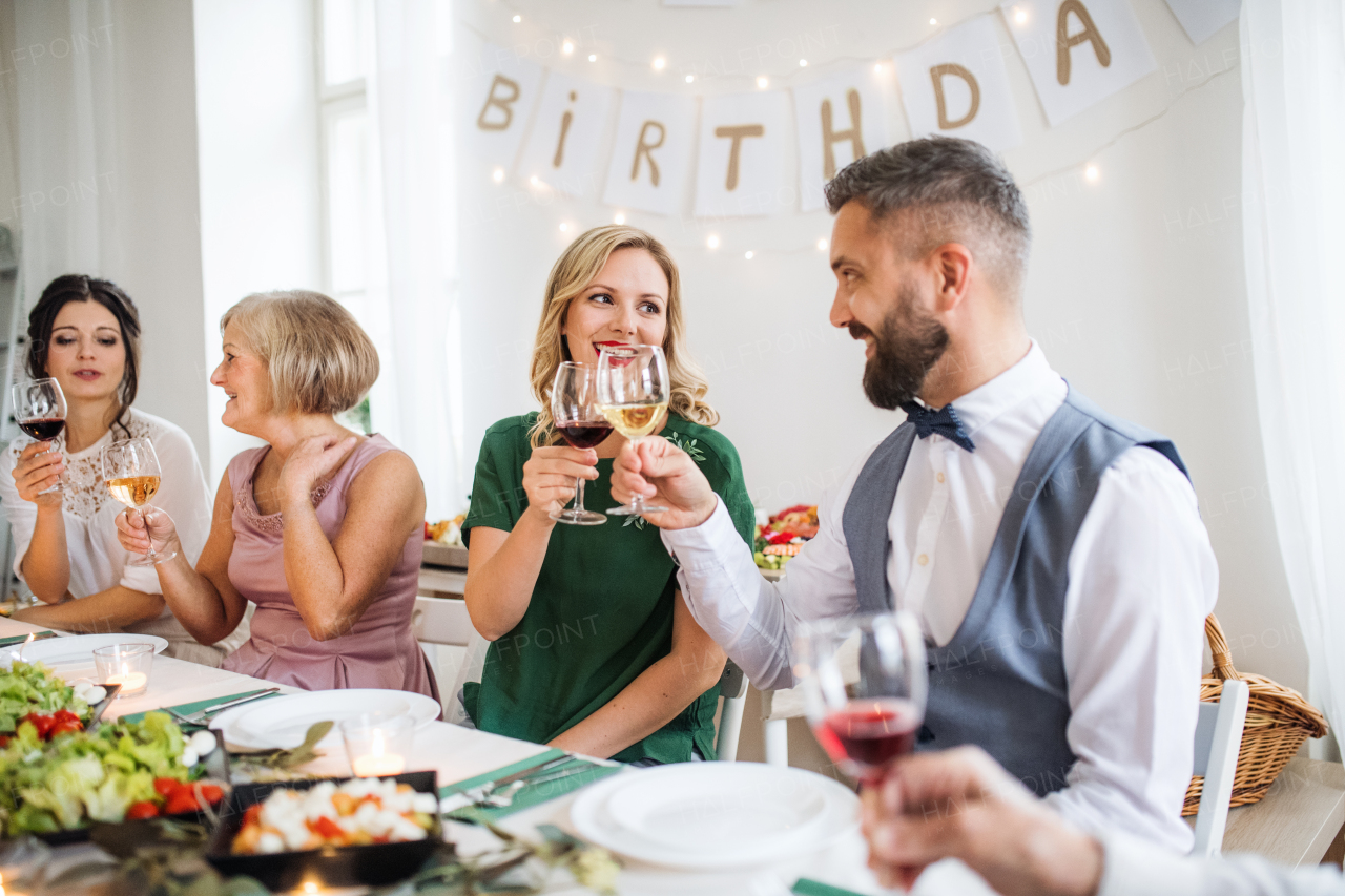 A big family sitting at a table on a indoor birthday party, clinking glasses with wine.