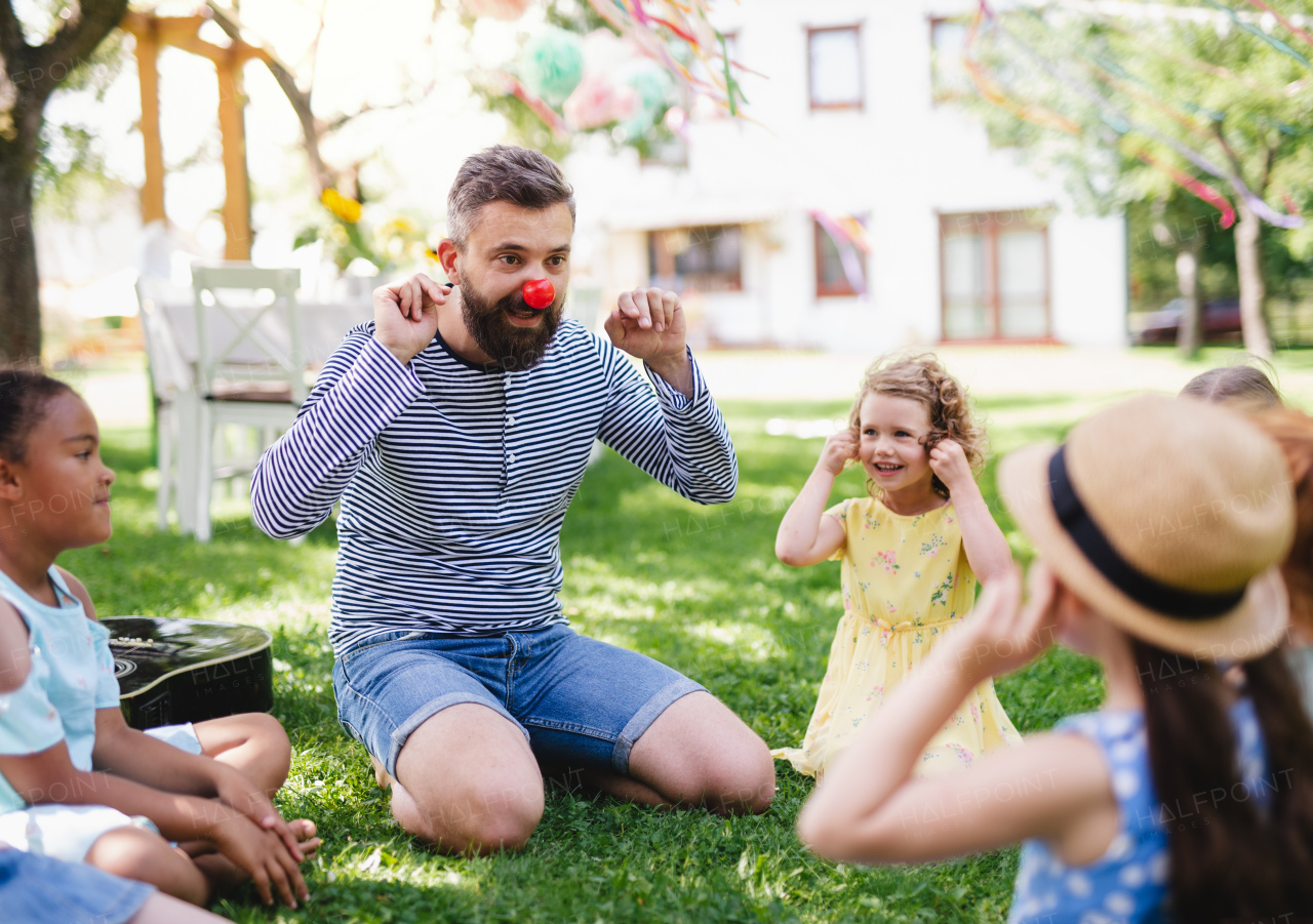 A man with small children sitting on ground outdoors in garden in summer, playing.