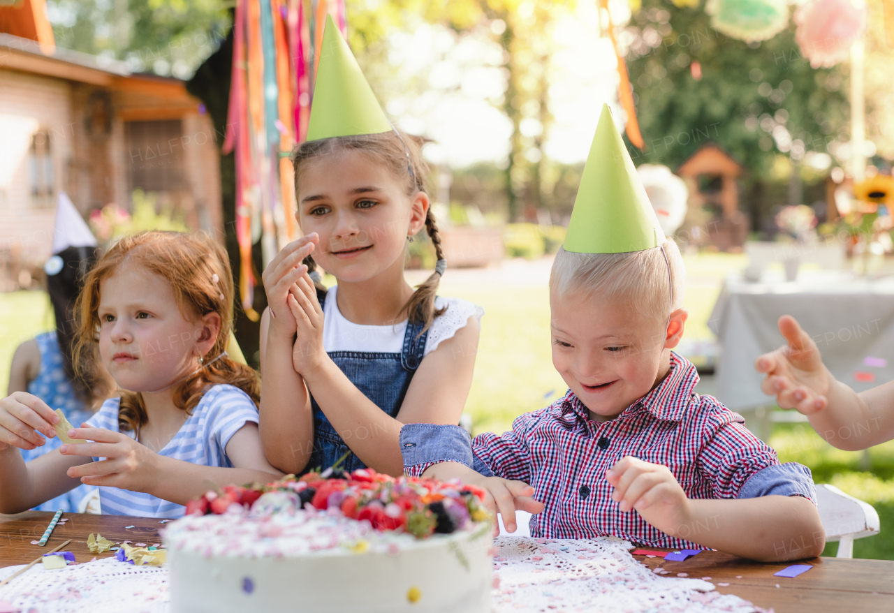 Down syndrome child with friends on birthday party outdoors in garden in summer.