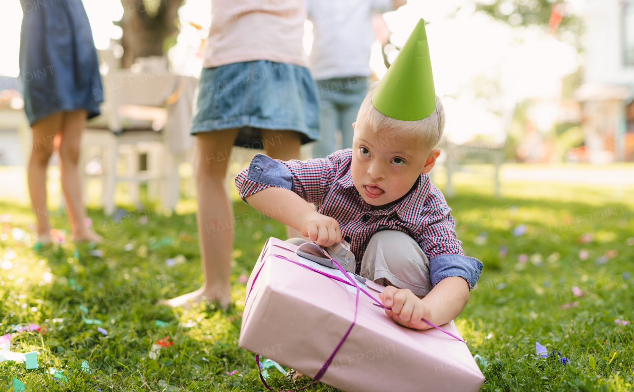 Down syndrome child with friends on birthday party outdoors in garden in summer, opening presents.