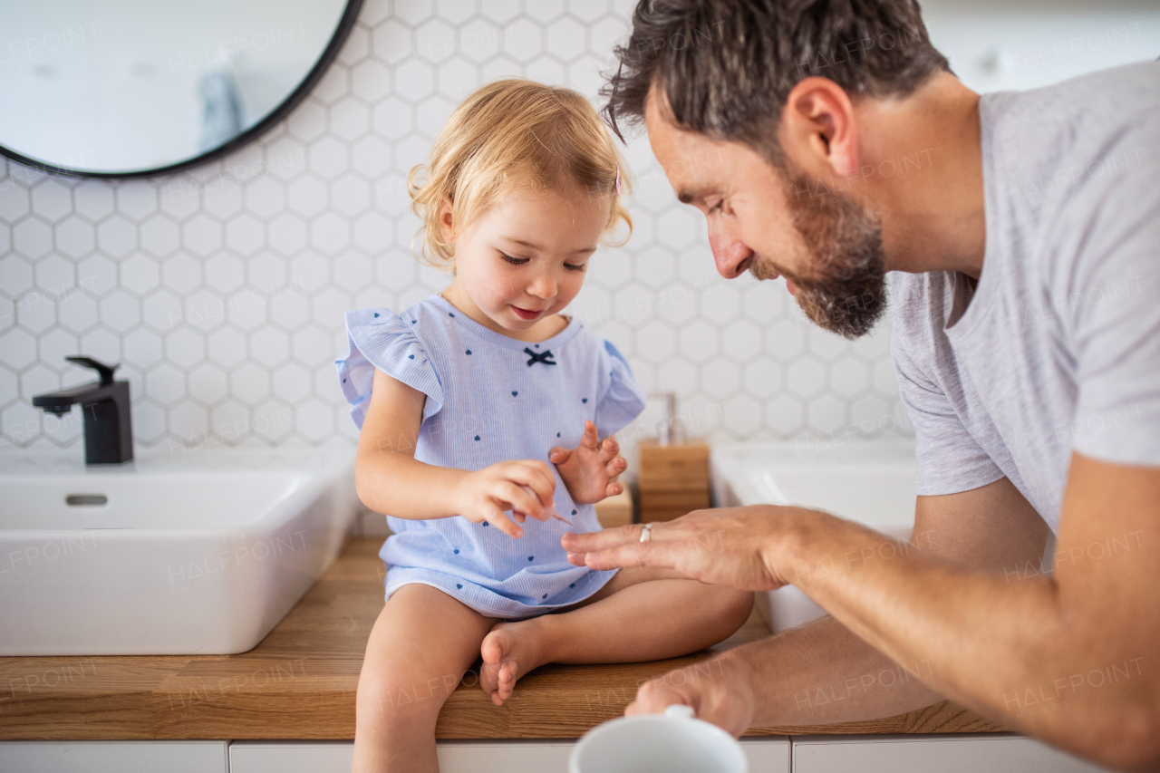 Mature father with small girl indoors in bathroom, painting nails.