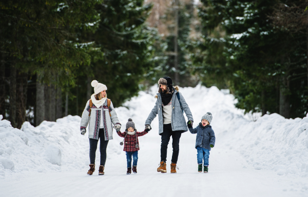 Front view portrait of father and mother with two small children in winter nature, walking in the snow.
