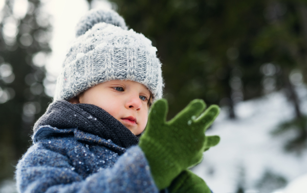 Happy small child standing in snow, holiday in winter nature.