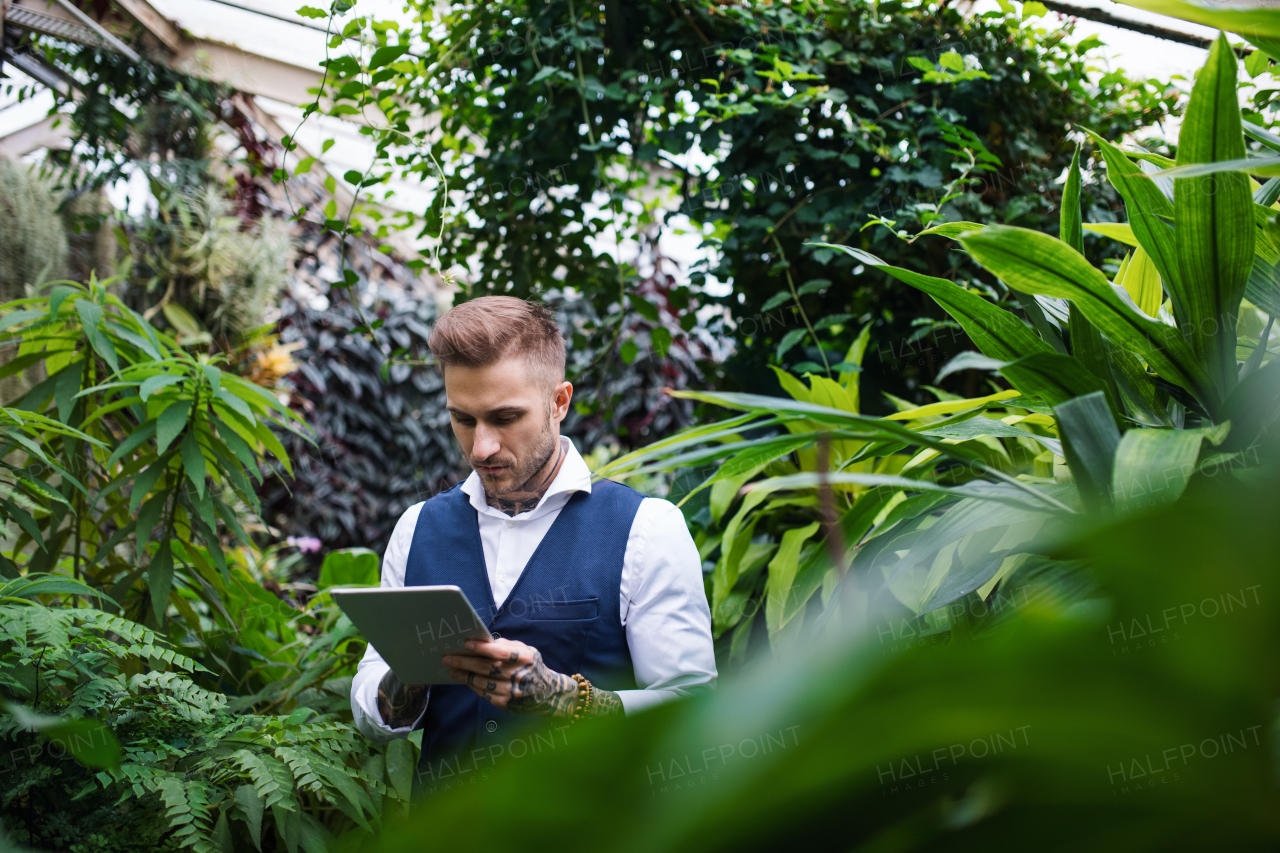 Young man with tablet standing in botanical garden, working. Green bussiness concept.