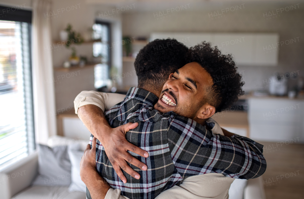 A young happy adult brothers in kitchen indoors at home, hugging.