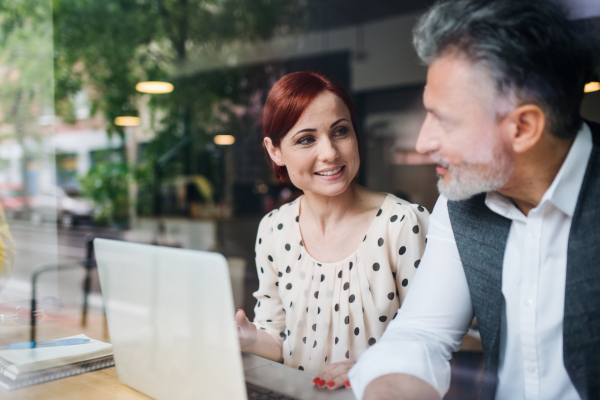 A man and woman having business meeting in a cafe, using laptop. Shot through glass.