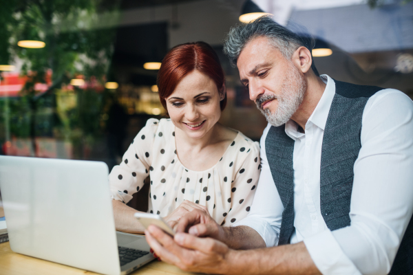 A man and woman having business meeting in a cafe, using laptop and smartpone. Shot through glass.