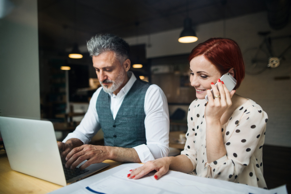 A man and woman having business meeting in a cafe, using laptop and smartphone.