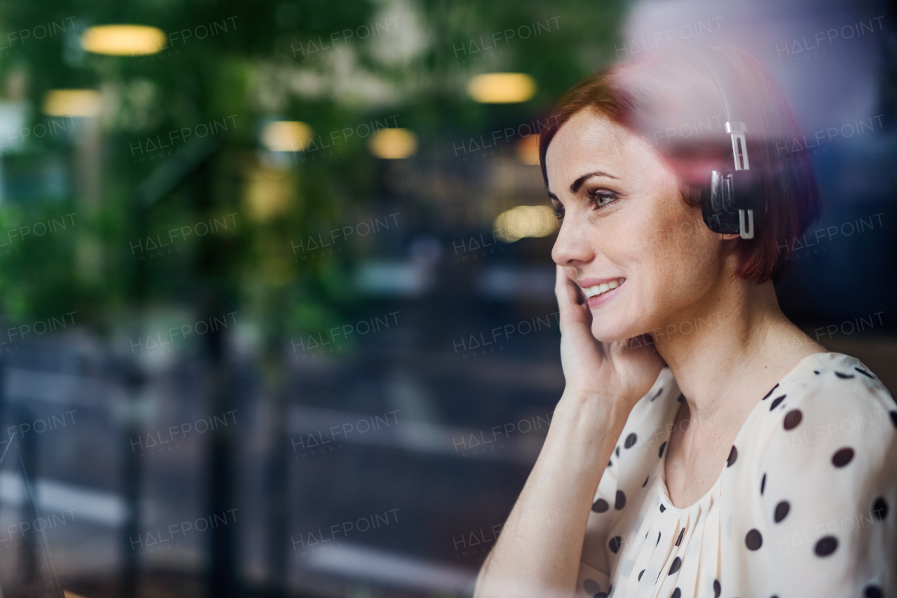 A portrait of woman with headphones sitting at the table in a cafe. Shot through glass.