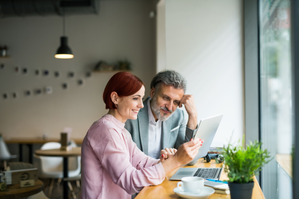 A man and woman having business meeting in a cafe, using laptop and tablet.