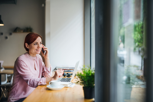 An attractive woman with coffee and telephone sitting at the table in a cafe, making a phone call.