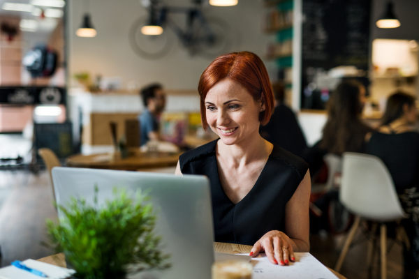 A portrait of attractive woman sitting at the table in a cafe, using laptop.