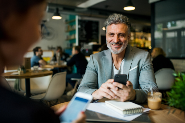 Man and unrecognizable woman having business meeting in a cafe, using smartphones.