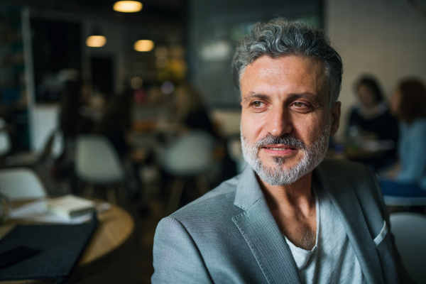 A portrait of a mature businessman in gray suit sitting in a cafe. Copy space.