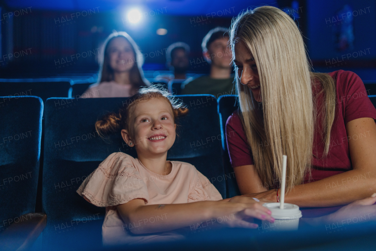 A happy small girl with mother in the cinema, watching film.
